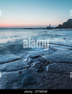 Vista dall'Old Hartley Bay Northumberland, Inghilterra, Regno Unito verso il faro di St Marys, Whitley Bay. All'alba. Foto Stock