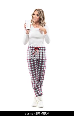 Giovane bella donna in pajama pubblicità bianco vuoto display smartphone che mostra alla fotocamera. Lunghezza totale del corpo isolata su sfondo bianco. Foto Stock