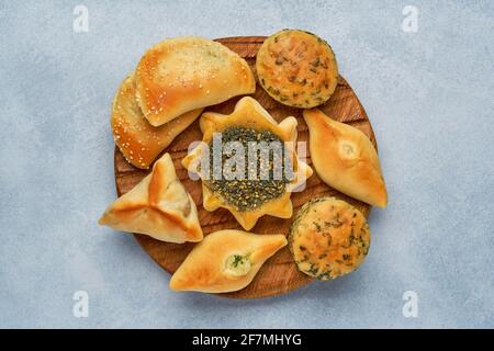 Pasticceria, fatayer o samosa, manaqeesh con zaatar e formaggio. Dolci assortiti con spinaci e patate su tavola di legno. Vista dall'alto Foto Stock