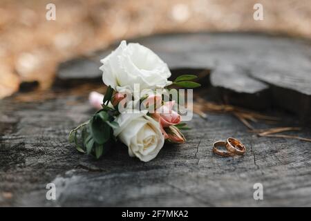 Primo piano di anelli di nozze e boutonnieres su sfondo di tessitura di legno Foto Stock