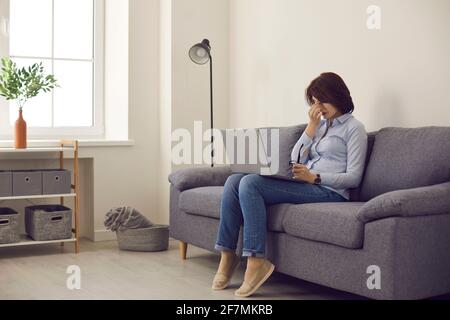 Donna stanca di lavorare su un computer portatile la toglie occhiali e strofina gli occhi Foto Stock