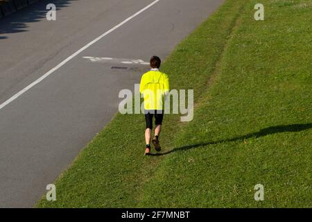 Lone giovane uomo che indossa una parte superiore gialla brillante jogging sopra Erba accanto a una pista ciclabile nel parco Las Llamas Mattina presto primavera Santander Cantabria Spagna Foto Stock