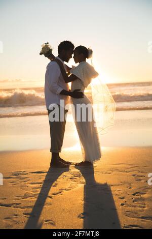 Felice coppia afroamericana in amore sposarsi, abbracciando sulla spiaggia durante il tramonto Foto Stock