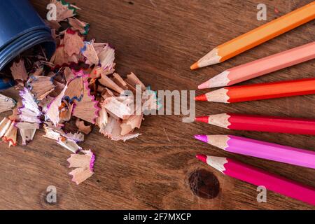 Matita matita matita rasature che fuoriescono da un affilatore a matita blu senza coperchio su una scrivania di legno duro, viola, arancione, rosa, giallo, matite allineate. Foto Stock