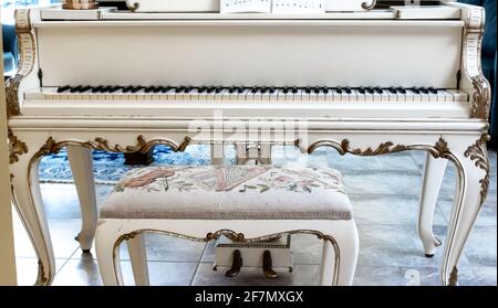 Un bel pianoforte bianco con tasti in avorio e una panca imbottita ornata su piastrelle beige. Interni, Londra, Canada. Scatto diretto. Foto Stock