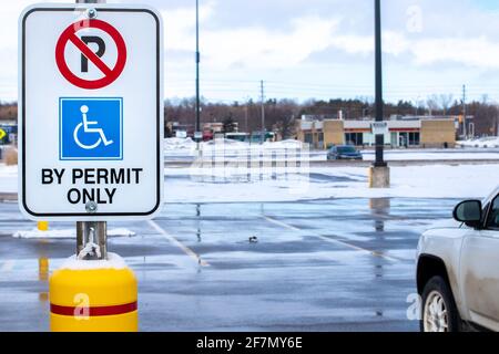 Parcheggio non disponibile, solo con cartello di permesso con il simbolo di accesso internazionale visualizzato su un cartello rettangolare verticale in un parcheggio ammaccato e innevato. Foto Stock