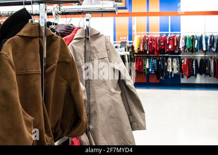 Una giacca in pelle scamosciata e un trench beige su una rastrelliera di abbigliamento in argento in un negozio Thrift a Londra, Ontario, Canada. Bokeh, sfondo a messa a fuoco morbida. Foto Stock