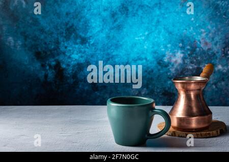 Preparare il caffè in un Turk. Teck in rame e tazza in ceramica. Sfondo blu luminoso. Foto Stock