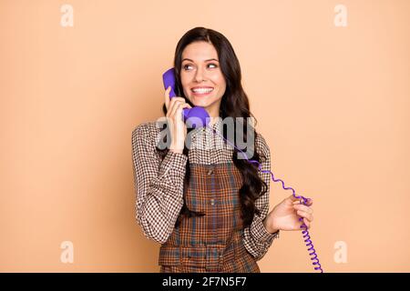 Ritratto di attraente allegra ragazza con capelli ondulati che chiama con il telefono vintage spazio di copia parlante isolato su sfondo color pastello beige Foto Stock