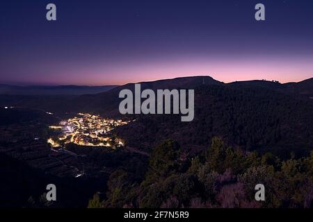 Piccolo villaggio in montagna di notte, cielo con stelle, primo piano di montagne, luci accese Foto Stock