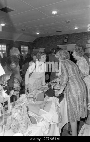 la gente che osserva gli articoli assortiti della seconda mano per la vendita a. tradizionale sala chiesa interna fete portare e acquistare jumble vendita fine anni '70 regno unito Foto Stock