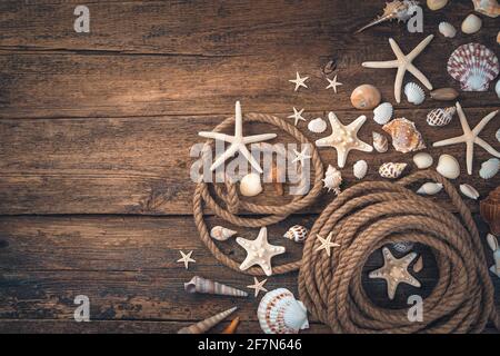 Conchiglie, stelle marine di vari tipi e forme, una corda su uno sfondo di legno marrone. Vista dall'alto, spazio di copia. Foto Stock