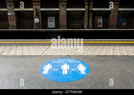 Il cartello sul pavimento della piattaforma alla stazione della metropolitana di Notting Hill Gate London avverte le persone a distanza sociale a causa del coronavirus. Foto Stock