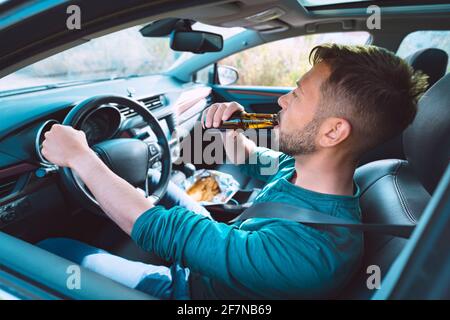 Guida ubriaca. Giovane uomo che beve birra durante la guida di un'auto. Conducente sotto l'influenza dell'alcol. Concetto di guida pericolosa. Foto Stock