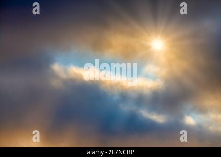 Un Sunburst di raggi di luce si rompe attraverso il luminoso Nuvole dettagliate Foto Stock
