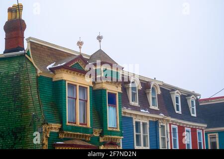 Finestre dormer decorative d'epoca su vecchi edifici in legno colorato. Le case esterne in legno sono di colore verde, blu e rosso. Foto Stock