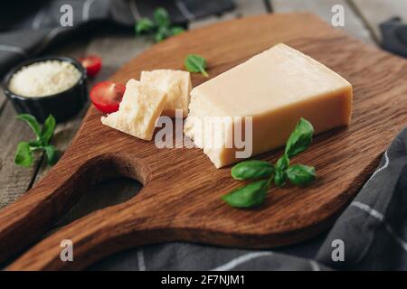 Concetto di cucina Italiana. Tagliere, pezzi di formaggio parmigiano, formaggio grattugiato in ciotola nera, tagli di pomodori ciliegini, rami di foglie di basilico, cucina Foto Stock