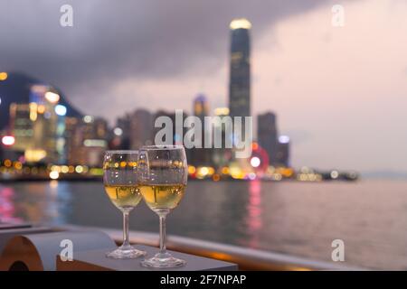 Due bicchieri di vino con scintillanti luci notturne della città in centro, Hong Kong Victoria Harbour come sfondo, concetto romantico per gli amanti e valente Foto Stock