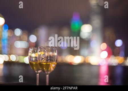 Due bicchieri di vino con scintillanti luci notturne della città in centro, Hong Kong Victoria Harbour come sfondo, concetto romantico per gli amanti e valente Foto Stock