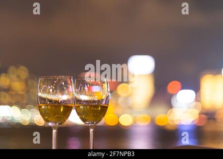 Due bicchieri di vino con scintillanti luci notturne della città in centro, Hong Kong Victoria Harbour come sfondo, concetto romantico per gli amanti e valente Foto Stock