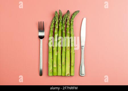 Asparagi con forchetta e coltello su fondo rosa. Asparagi vegetali freschi per una dieta e una nutrizione sana. Verdure e concetto di cibo sano. Foto di alta qualità Foto Stock