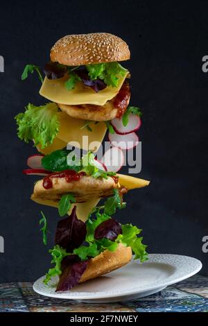 Levitating fette di hamburger. Cibo di volo. Hamburger Bun, cotoletta di pollo doppia con formaggio, lattuga, rucola e rafano. Carne, verdure e pane. Ingredienti su sfondo nero. Foto Stock