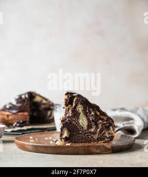 Pezzo di torta di marmo fatta in casa con glassa di cioccolato e noci su piastra di legno. Torta di zebra alla vaniglia al cioccolato. Messa a fuoco selettiva. Foto Stock