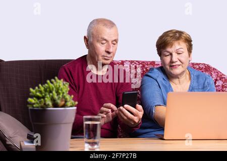 Felice coppia senior che usa il telefono e il computer portatile per effettuare un ordine online. Foto Stock