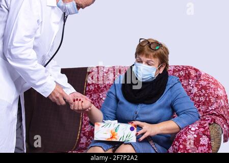 Medico maschile consolante una donna anziana che indossa una maschera facciale durante una visita a casa Foto Stock