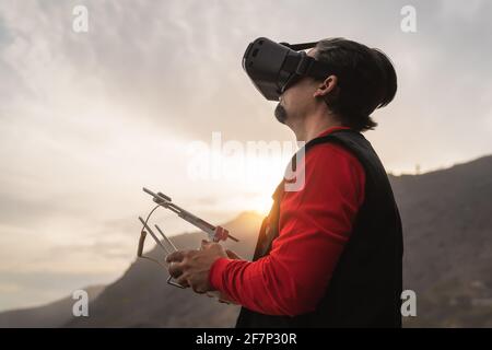 Pilota professionista di droni maschile che fa esperienza fpv con la realtà virtuale Occhiali durante il tramonto - tecnologia e concetto di innovazione Foto Stock