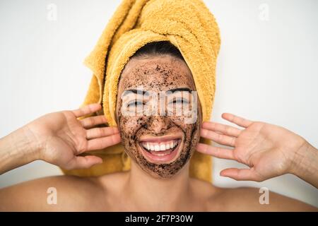 Giovane donna sorridente che applica la maschera di scrub del caffè sul viso - ragazza felice che ha la cura della pelle spa giorno a casa Foto Stock