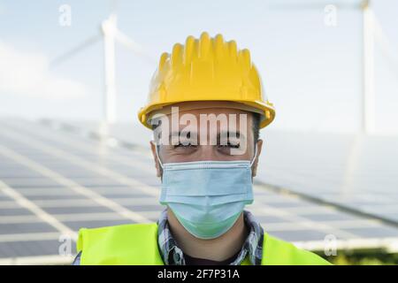Giovane ingegnere che lavora per l'energia alternativa con turbina eolica e. pannello solare mentre si indossa la maschera facciale durante l'epidemia di virus corona Foto Stock