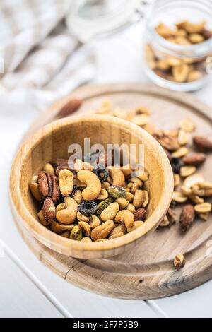 Mescolare le noci salate in un recipiente di legno su un tavolo bianco. Foto Stock