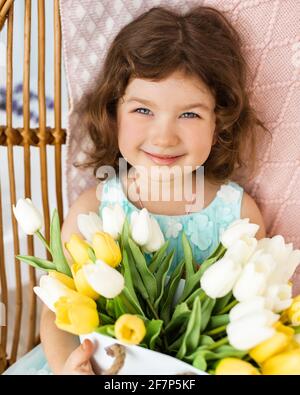 Primo piano Foto di bella ragazza 4-5 anni con tulipani gialli, guardando la macchina fotografica e sorridendo Foto Stock