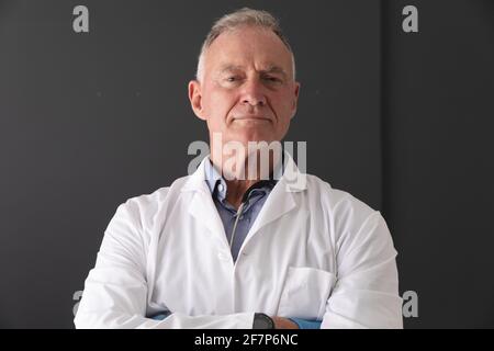 Ritratto di dottore caucasico di sesso maschile superiore con cappotto bianco in piedi con le braccia incrociate, sorridente Foto Stock