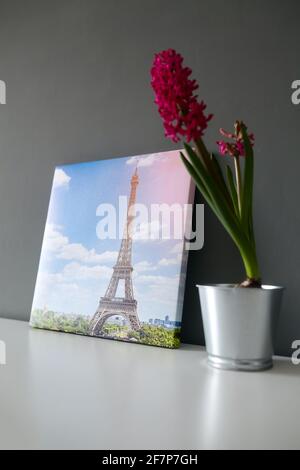 Stampa su tela allungata sulla cornice con gallery wrap su sfondo grigio della parete. Fotografia con il paesaggio urbano della Torre Eiffel di Parigi e fiore in vaso su cenere bianca Foto Stock