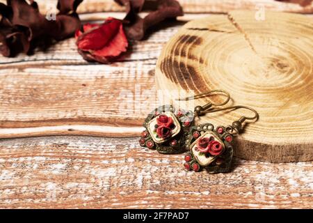 Orecchini d'oro vintage con rose rosse su tavolo di legno, con cuscinetto di legno e petali rossi Foto Stock