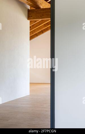 Particolare di una porta aperta, camera bianca vuota con travi in legno a vista e pavimenti in legno massello. Nessuno all'interno. Foto Stock