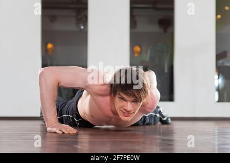 Uomo muscolare esercizio facendo pushups con un solo braccio in una palestra Foto Stock