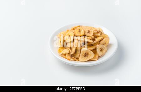 Pezzi di banane essiccate in una piastra bianca su uno sfondo chiaro. Chip di banana. Vista laterale, spazio di copia. Foto Stock