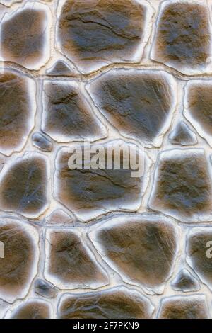 La struttura di un muro di cemento nello stile di una pelle di serpente color palude, pavimentata con grandi ciottoli. Primo piano. Foto Stock