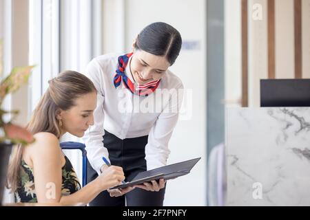 donna turistica che va a riempire e firmare il modulo di registrazione del check-in dell'hotel al banco della reception, kundenservice quando arrivo destinazione per la vacanza estiva Foto Stock