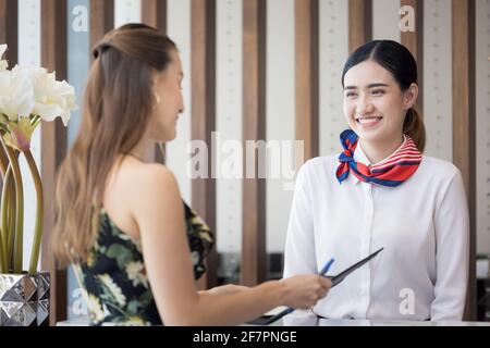 donna turistica che va a riempire e firmare il modulo di registrazione del check-in dell'hotel al banco della reception, kundenservice quando arrivo destinazione per la vacanza estiva Foto Stock