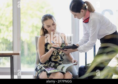donna turistica che va a riempire e firmare il modulo di registrazione del check-in dell'hotel al banco della reception, kundenservice quando arrivo destinazione per la vacanza estiva Foto Stock