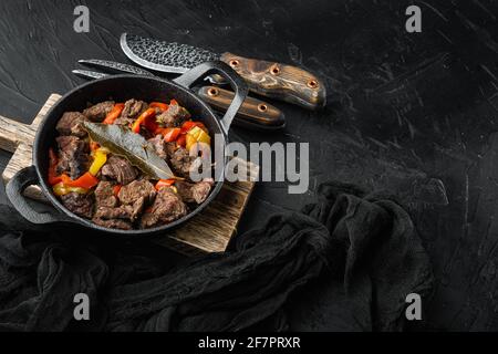 Stufato di carne e verdure servito, in padella di ghisa, su fondo di pietra nera, con spazio per la copia del testo Foto Stock