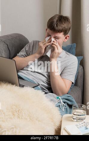 L'adolescente cerca di studiare online e si starnutisce in carta asciugamano. Autoisolamento. Quarantena. elearning a distanza. Foto Stock
