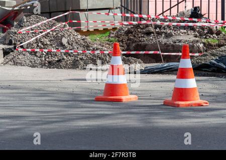 Coni di traffico arancione brillante che si trovano in fila su asfalto scuro. Buca sulla strada con un cono arancione. Foto Stock