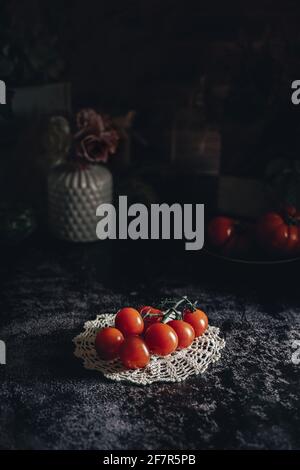 Moody fotografia di cibo scuro di pomodori ciliegini freschi sulla vite. Immagine di natura morta con un aspetto vintage e uno sfondo nero.