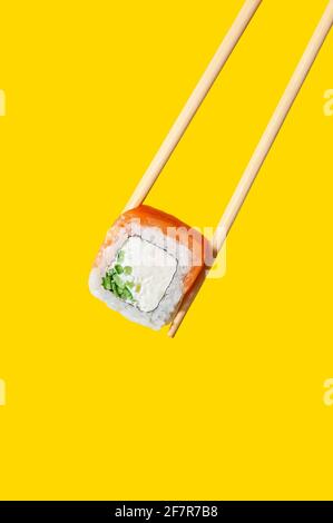 Primo piano su Philadelphia Roll con pesce salmone, formaggio e cetriolo su bastoncini di pesce su sfondo giallo. Foto Stock