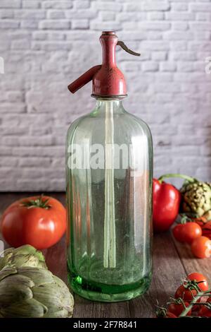 Fotografia di un antico sifone di soda, pomodori ciliegini freschi, posate antiche, carciofi e pepe rosso su un tavolo di legno. Immagine di natura morta Foto Stock